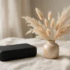 Étui discret noir et vase en céramique avec fleurs séchées sur un linge clair, ambiance élégante